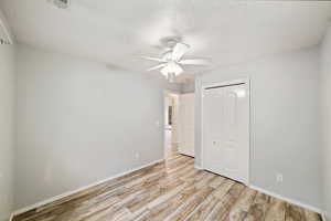 Unfurnished bedroom featuring a closet, light wood-type flooring, a ceiling fan, and a textured ceiling