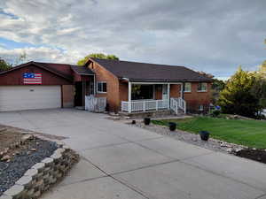 Ranch-style house with driveway, brick siding, a front yard, covered porch, and a garage