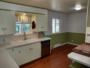 Kitchen with a wainscoted wall, light countertops, dark wood-style flooring, dishwasher, and white cabinetry