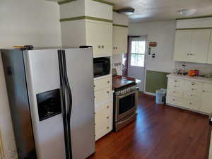 Kitchen featuring stainless steel appliances, a wainscoted wall, dark wood-type flooring, light countertops, and cream cabinetry