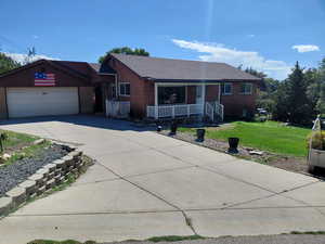 Ranch-style home featuring a front lawn, driveway, brick siding, a porch, and roof with shingles
