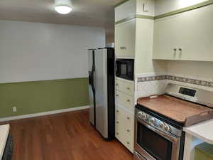 Kitchen featuring appliances with stainless steel finishes, wainscoting, dark wood-style floors, light countertops, and white cabinets