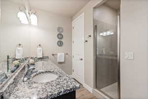 Bathroom featuring a stall shower, double vanity, light wood-style floors, and a chandelier