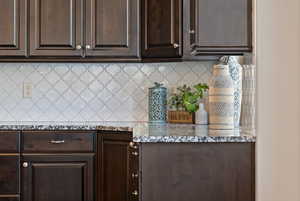 Kitchen with dark brown cabinets, tasteful backsplash, and light stone countertops