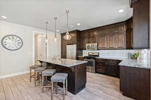 Kitchen featuring light stone counters, stainless steel appliances, tasteful backsplash, an island with sink, and recessed lighting