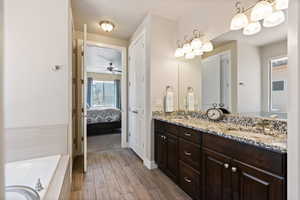 Full bathroom featuring double vanity, a bath, wood finish floors, a ceiling fan, and ensuite bath