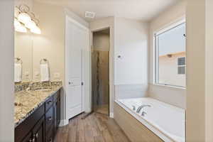 Full bathroom featuring double vanity, a garden tub, light wood-style floors, and a shower stall