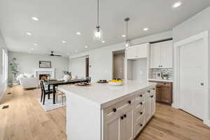 Kitchen with white cabinetry, light wood-style flooring, hanging light fixtures, open floor plan, and recessed lighting