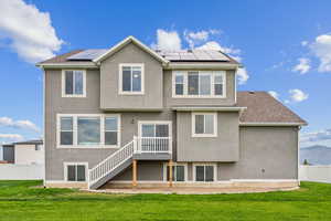 Rear view of property featuring stucco siding, a shingled roof, solar panels, and stairs
