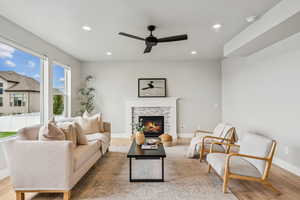 Living room featuring a stone fireplace, ceiling fan, recessed lighting, and light wood finished floors