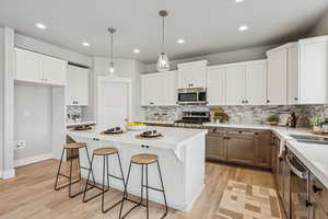 Kitchen with a kitchen bar, white cabinetry, decorative backsplash, decorative light fixtures, and stainless steel appliances