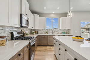 Kitchen with white cabinetry, stainless steel appliances, hanging light fixtures, light wood-style flooring, and light stone countertops