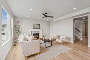 Living room featuring stairs, recessed lighting, a ceiling fan, a stone fireplace, and light wood finished floors