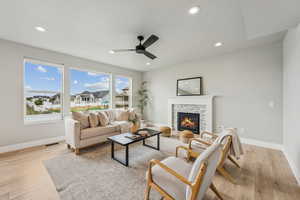 Living room with a stone fireplace, light wood-style floors, recessed lighting, and a ceiling fan