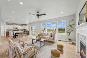 Living area with light wood-style flooring, a glass covered fireplace, recessed lighting, and ceiling fan
