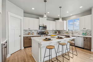 Kitchen featuring white cabinetry, stainless steel appliances, a kitchen bar, light wood-style floors, and hanging light fixtures