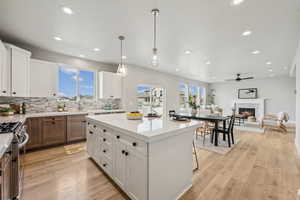 Kitchen with white cabinetry, gas stove, hanging light fixtures, backsplash, and open floor plan