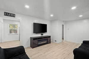 Living room featuring light wood finished floors, a glass covered fireplace, and recessed lighting