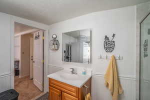 Full bath featuring vanity, wainscoting, a textured ceiling, and a shower stall