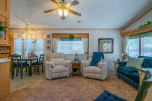 Living room with healthy amount of natural light, light carpet, ornamental molding, lofted ceiling, and ceiling fan