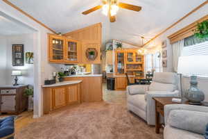 Living room featuring vaulted ceiling, crown molding, a ceiling fan, a chandelier, and light colored carpet