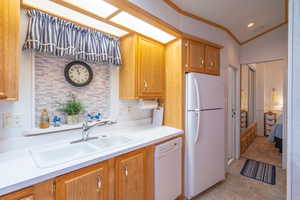 Kitchen with white appliances, light countertops, ornamental molding, and brown cabinetry