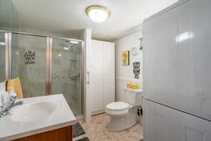 Full bath featuring vanity, a stall shower, a textured ceiling, light tile patterned floors, and a wainscoted wall