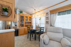 Dining area featuring vaulted ceiling, healthy amount of natural light, light stone finish floors, crown molding, and a chandelier