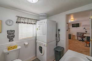 Full bathroom with a textured ceiling, stacked washing machine and dryer, and a wainscoted wall
