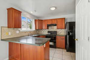 Kitchen featuring black appliances, a peninsula, decorative backsplash, brown cabinets, and dark countertops