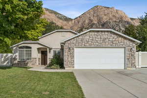 Ranch-style house with stone siding, driveway, a garage, a mountain view, and stucco siding
