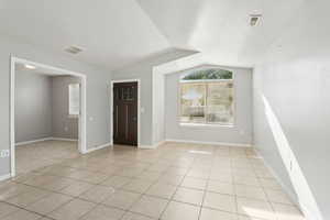 Unfurnished room featuring light tile patterned floors, vaulted ceiling, and a textured ceiling
