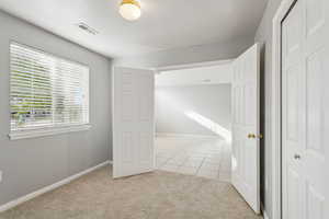 Unfurnished bedroom with light carpet, light tile patterned flooring, and a closet