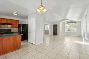 Kitchen featuring light tile patterned flooring, decorative light fixtures, dark countertops, tasteful backsplash, and black appliances