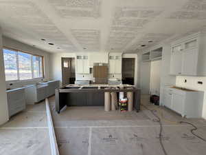 Kitchen featuring a kitchen island, glass insert cabinets, white cabinets, a textured ceiling, and a kitchen breakfast bar