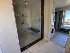 Full bathroom featuring a marble finish shower, light marble finish flooring, stacked washer and dryer, a textured ceiling, and a walk in closet