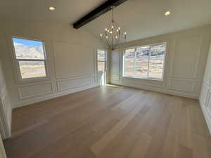 Primary Bedroom featuring a decorative wall, lofted ceiling with beams, a chandelier, and light wood-style flooring