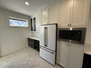Butler Pantry with refrigerator, a textured ceiling, stainless steel microwave, glass insert cabinets, and dual tone cabinetry