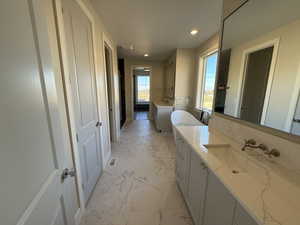 Full bath featuring a freestanding tub, two vanities, light marble finish floors, and recessed lighting