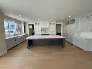 Dual tone kitchen featuring a kitchen breakfast bar, backsplash, glass insert cabinets, dual tone cabinets, and a large island