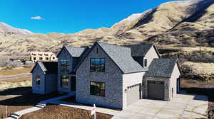 View of front of home featuring concrete driveway, stone siding, a high end roof, a mountain view, and a garage