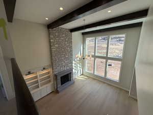 Unfurnished living room featuring suspended lighting, a stone fireplace, light wood-style flooring, and beam ceiling