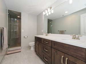 Bathroom featuring double vanity, a shower stall, and a textured ceiling