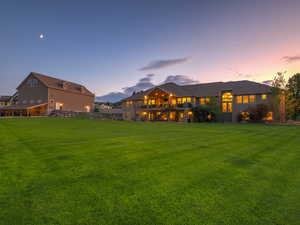 Back of property at dusk with a yard and a balcony