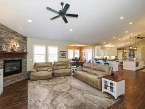Living area featuring ceiling fan, arched walkways, vaulted ceiling, a stone fireplace, and recessed lighting