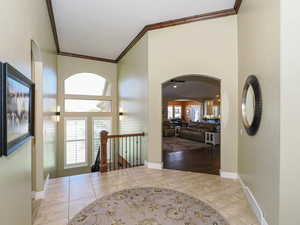 Entrance foyer with arched walkways, light tile patterned flooring, crown molding, and a towering ceiling