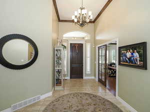 Foyer entrance featuring a high ceiling, light tile patterned floors, french doors, ornamental molding, and a chandelier