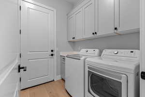 Washroom with light wood finished floors, cabinet space, and independent washer and dryer