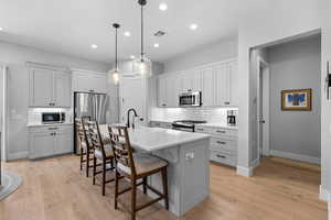 Kitchen featuring a kitchen bar, tasteful backsplash, appliances with stainless steel finishes, decorative light fixtures, and a center island with sink