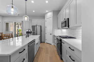 Kitchen with a kitchen island with sink, stainless steel appliances, hanging light fixtures, recessed lighting, and light wood-type flooring